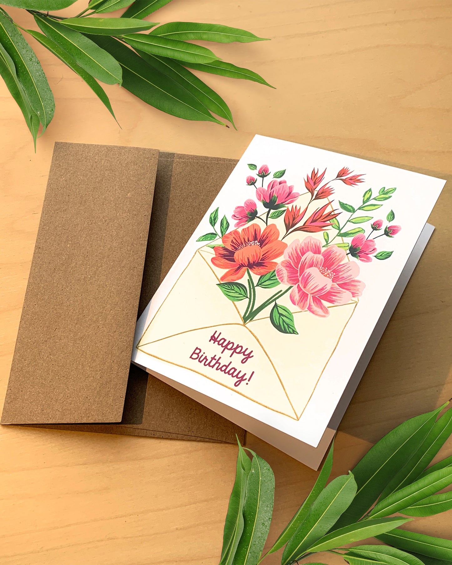 Greeting card with floral design and 'Happy Birthday!' text on a wooden surface with green leaves.
