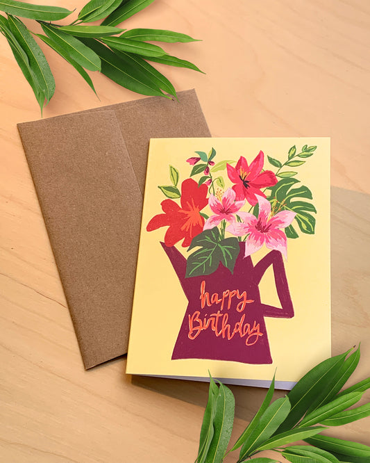 Birthday card with floral design and brown envelope on a wooden surface