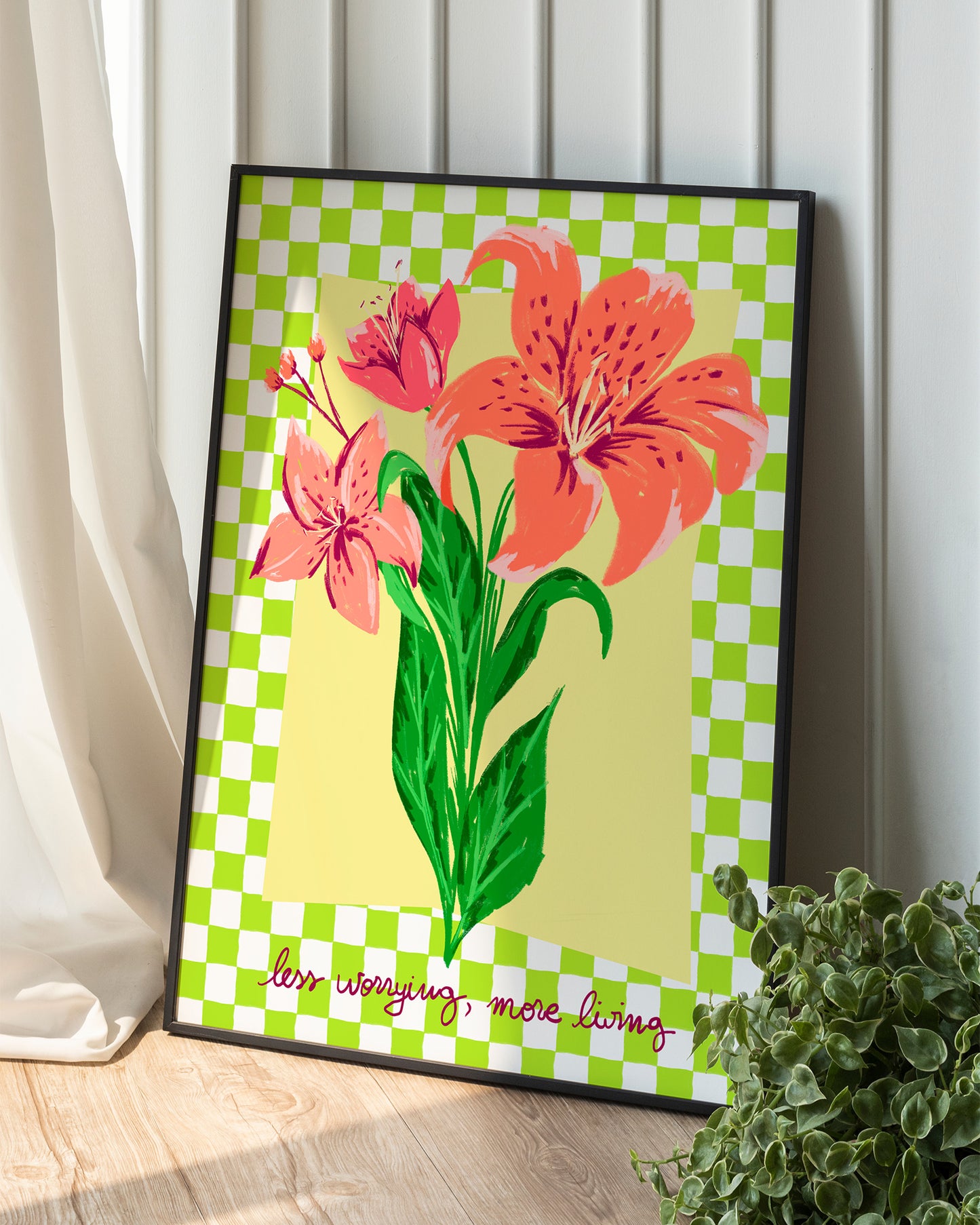 Framed artwork with pink flowers on a green and white checkered background, placed on a wooden surface.