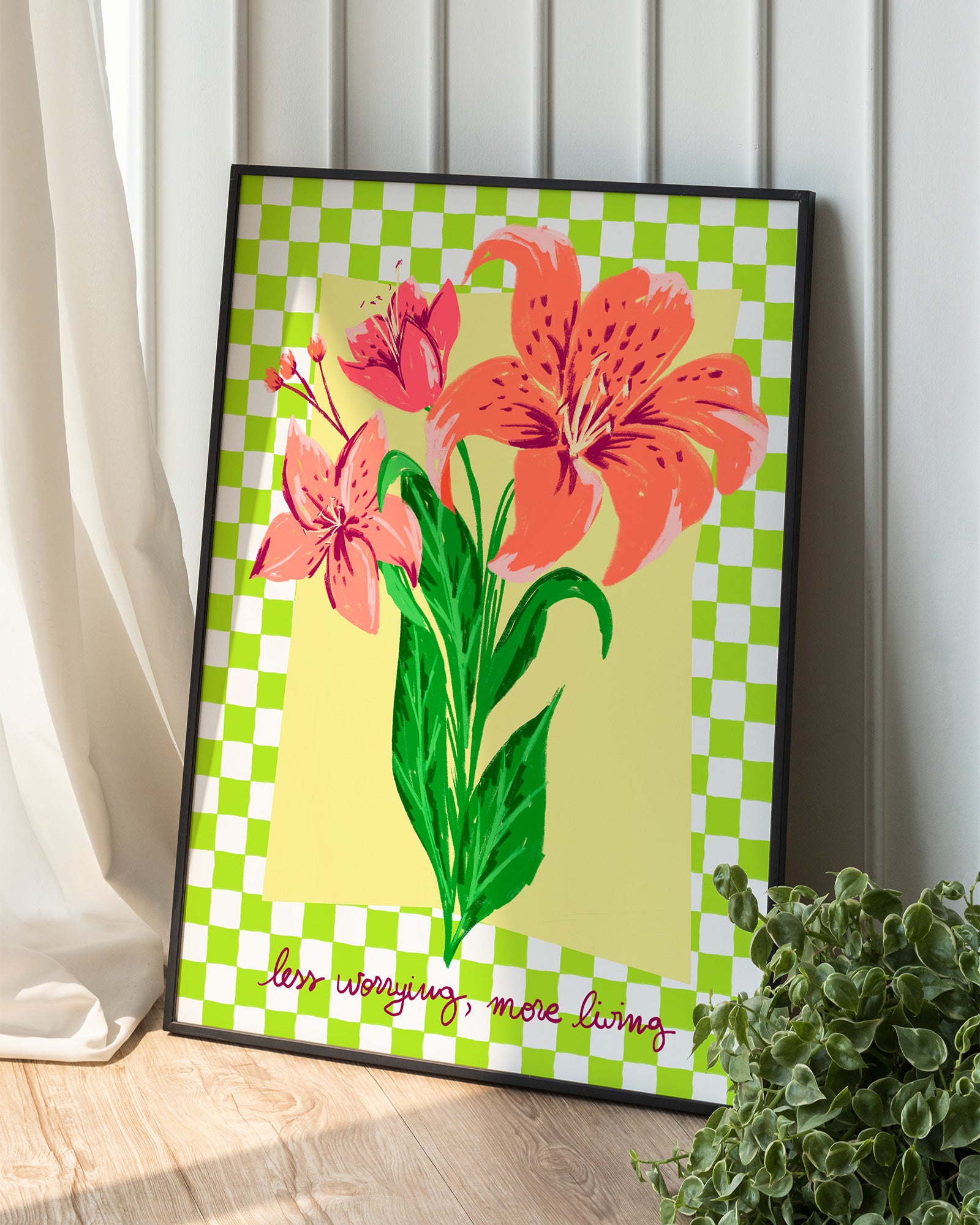 Framed artwork with pink flowers on a green and white checkered background, placed on a wooden surface.