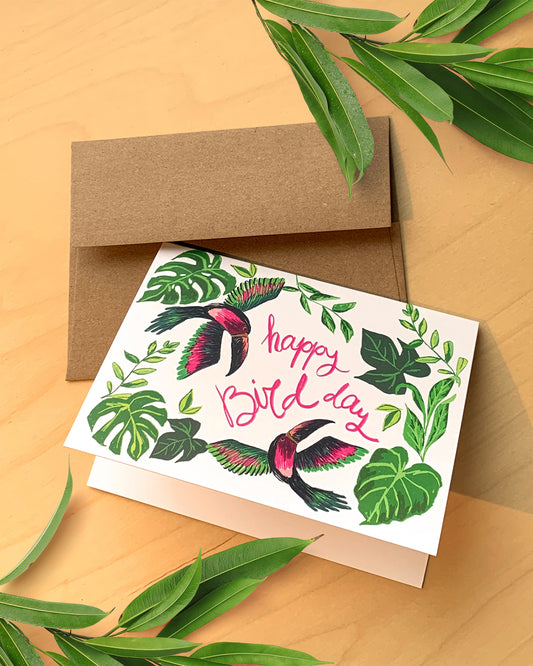 Greeting card with birds and leaves design, accompanied by a brown envelope on a wooden surface.
