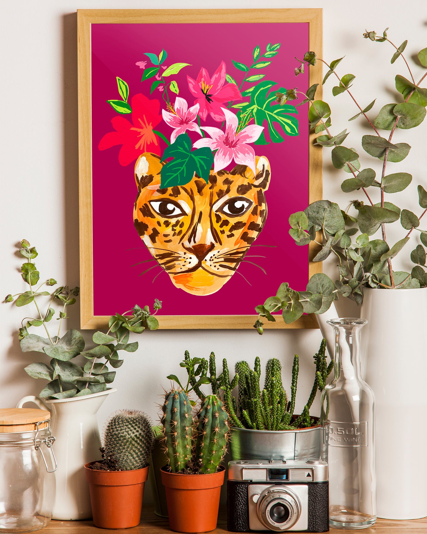 Framed artwork of a leopard with flowers on a pink background, surrounded by potted plants.
