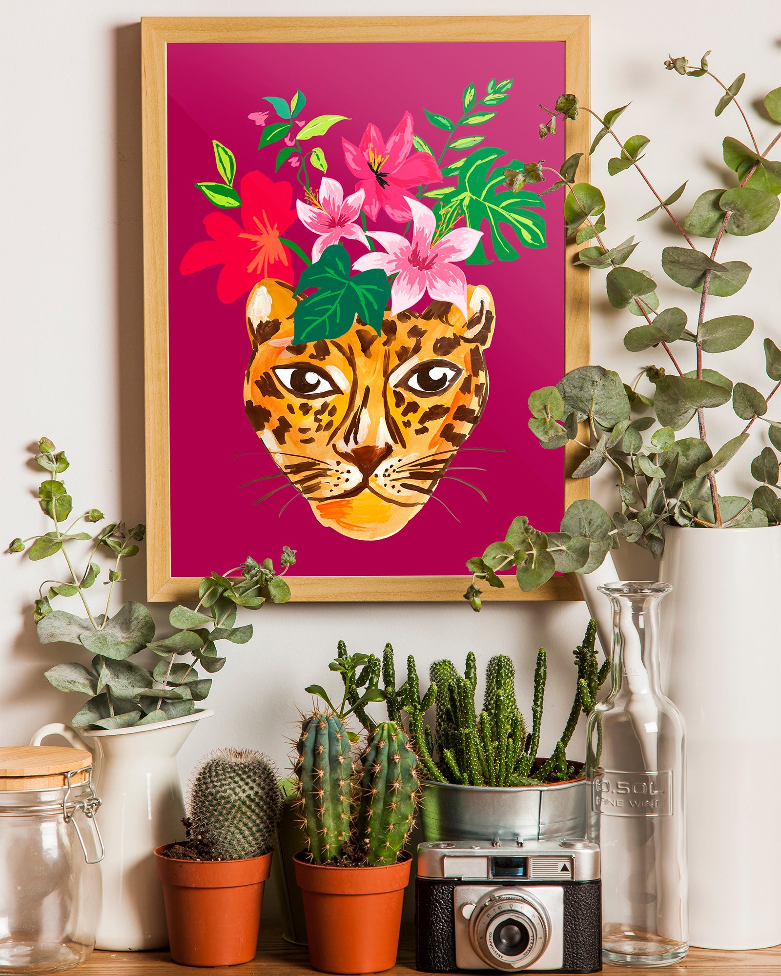 Framed artwork of a leopard with flowers on a pink background, surrounded by potted plants.
