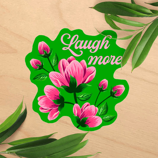 Decorative sign with pink flowers and 'Laugh more' text on a wooden background with leaves.